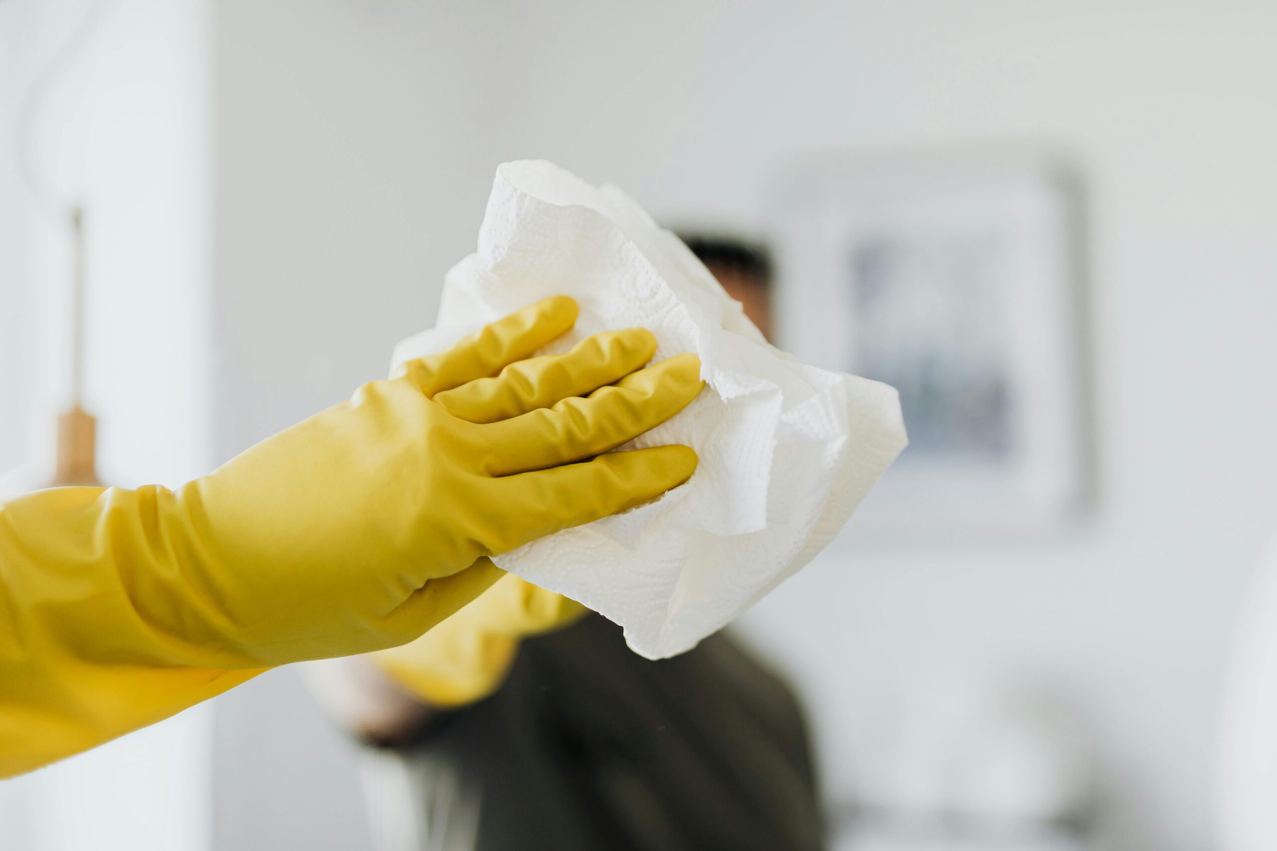 Home Faceless male wearing yellow latex gloves and wiping mirror with paper napkin in bathroom while cleaning and disinfects house